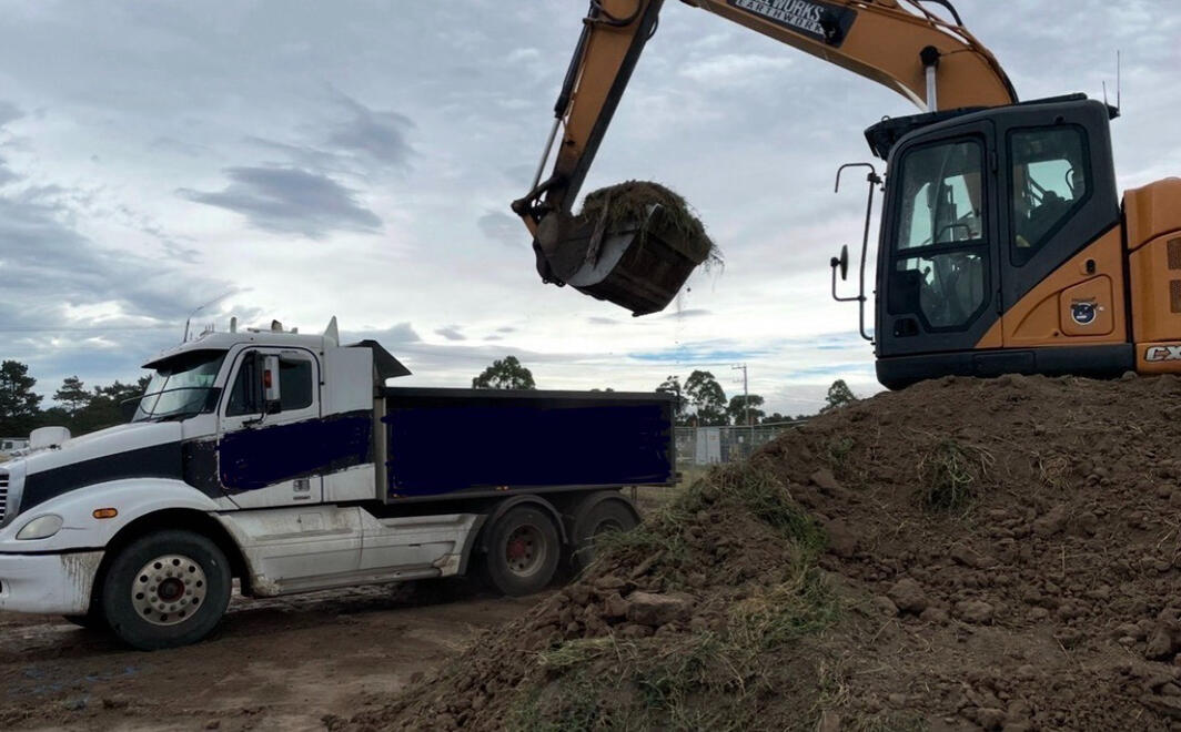 Excavator Loading Work Truck – All Equipped Plant Hire Excavator placing soil into a truck during earthmoving.